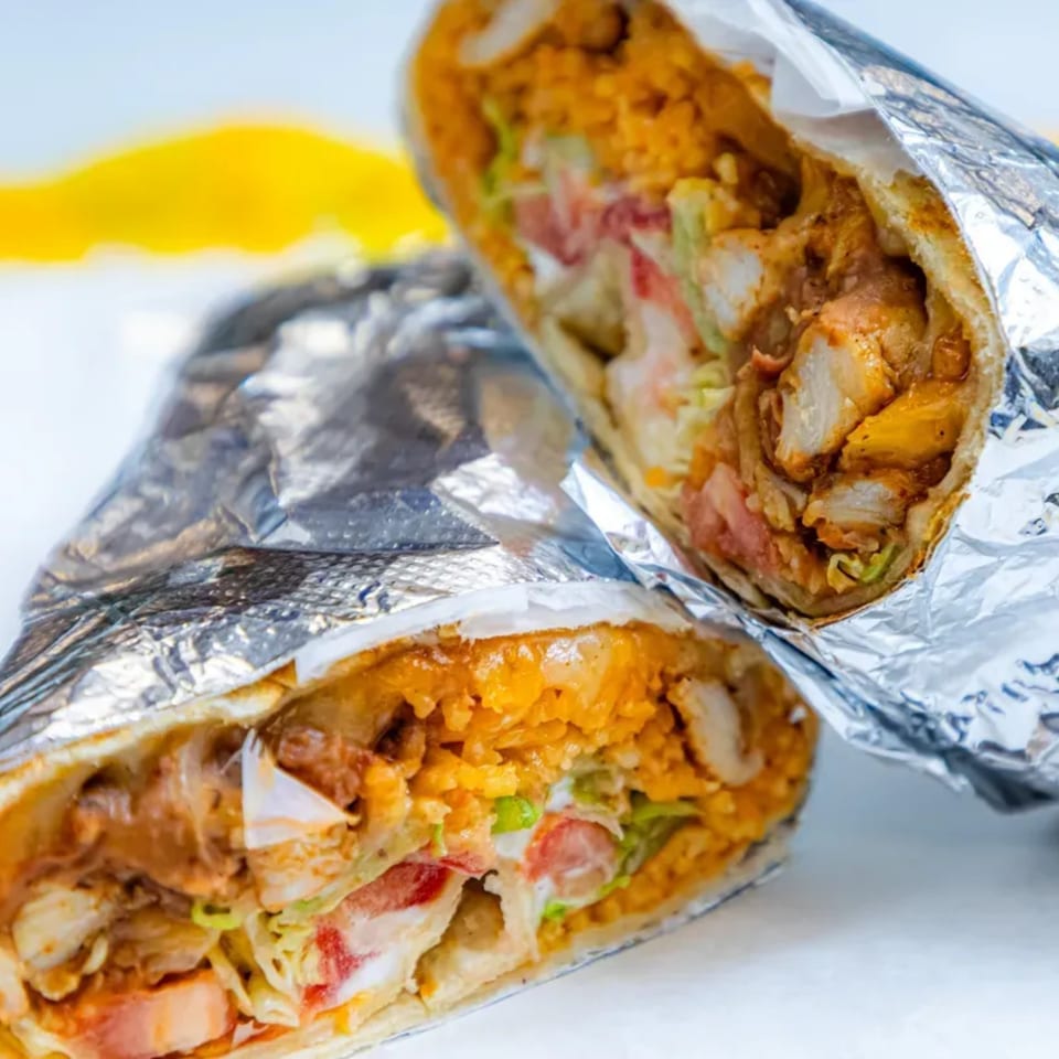 Two foil-wrapped burritos, cut in half, revealing chicken, rice, lettuce, and tomato filling.