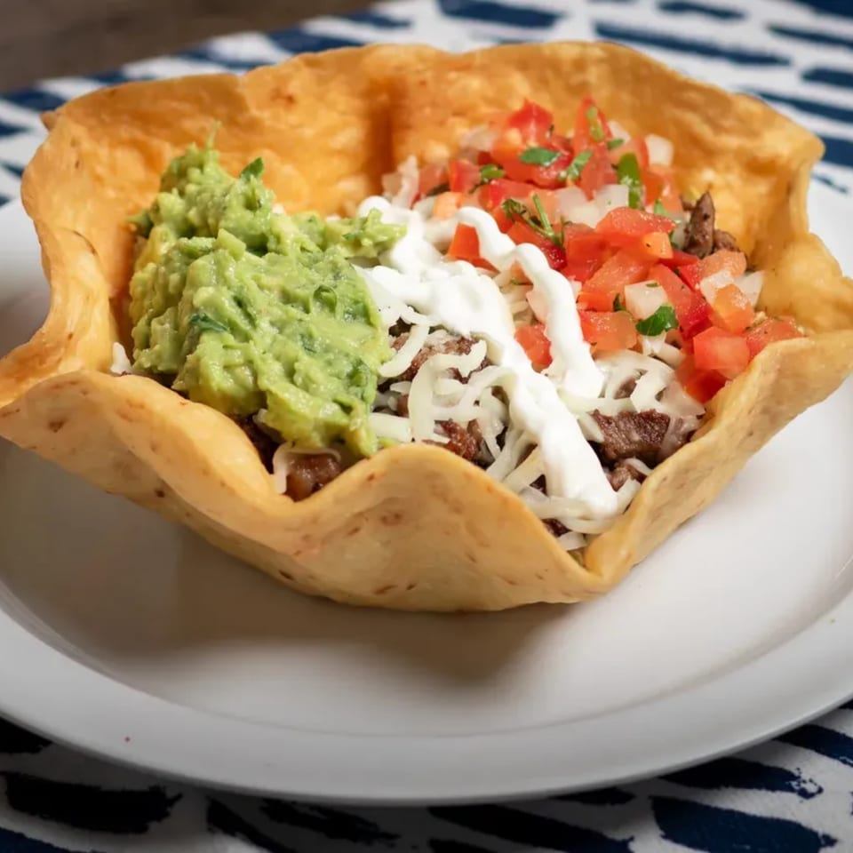 A taco salad in a crispy tortilla bowl with guacamole, sour cream, cheese, and pico de gallo.