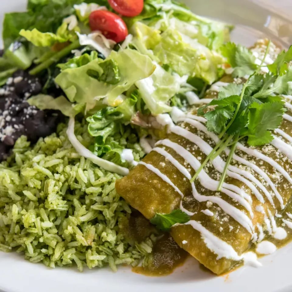 Two green enchiladas with sour cream, cilantro, green rice, black beans, and salad.