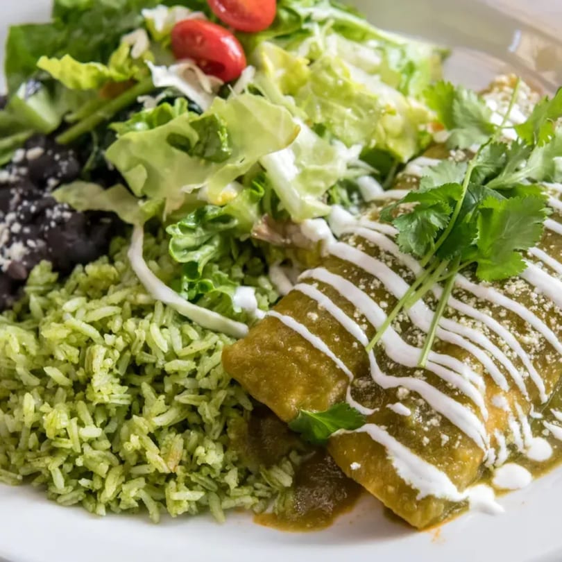 Two green enchiladas with sour cream, cilantro, green rice, black beans, and salad.