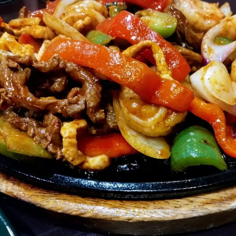 Sizzling fajitas with beef, chicken, shrimp, red and green peppers, and onions on a hot plate.