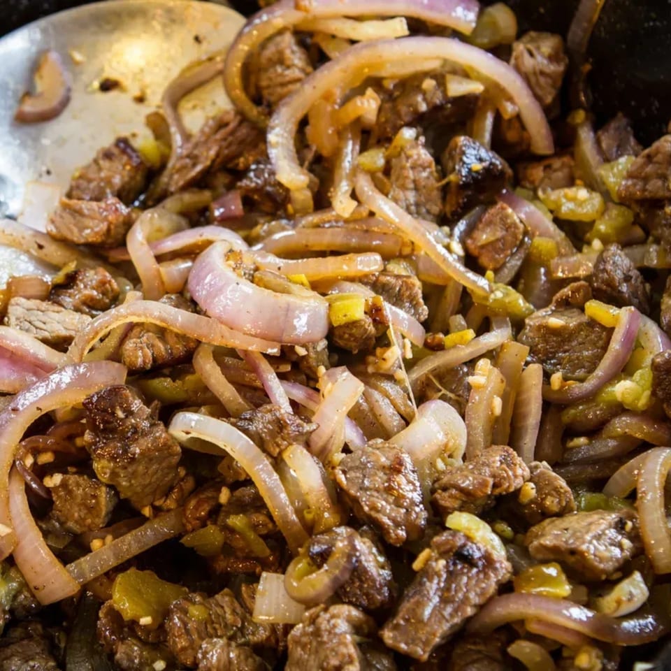 Close-up of sizzling beef and onions with green peppers in a pan, ready to serve.