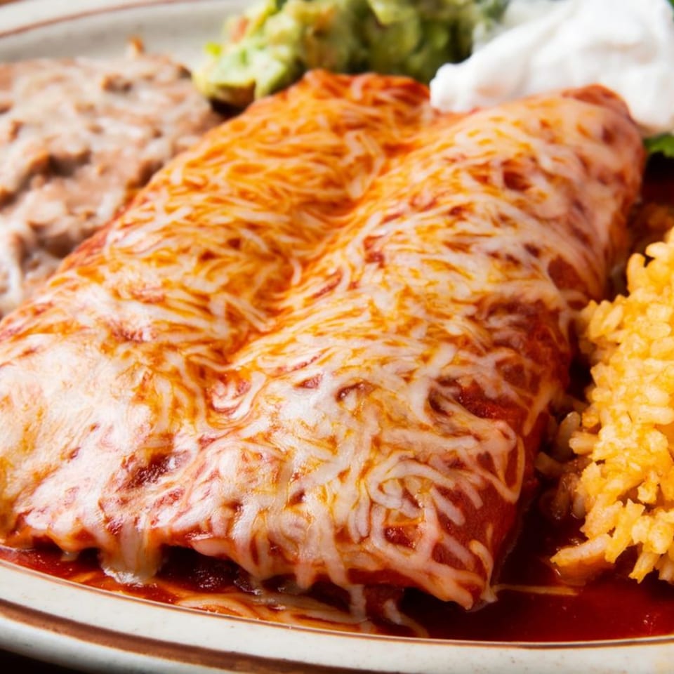 Two cheesy enchiladas with red sauce, refried beans, rice, guacamole, and sour cream.