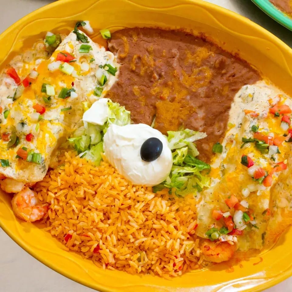 Two enchiladas with shrimp, rice, refried beans, sour cream, and lettuce on a yellow plate.