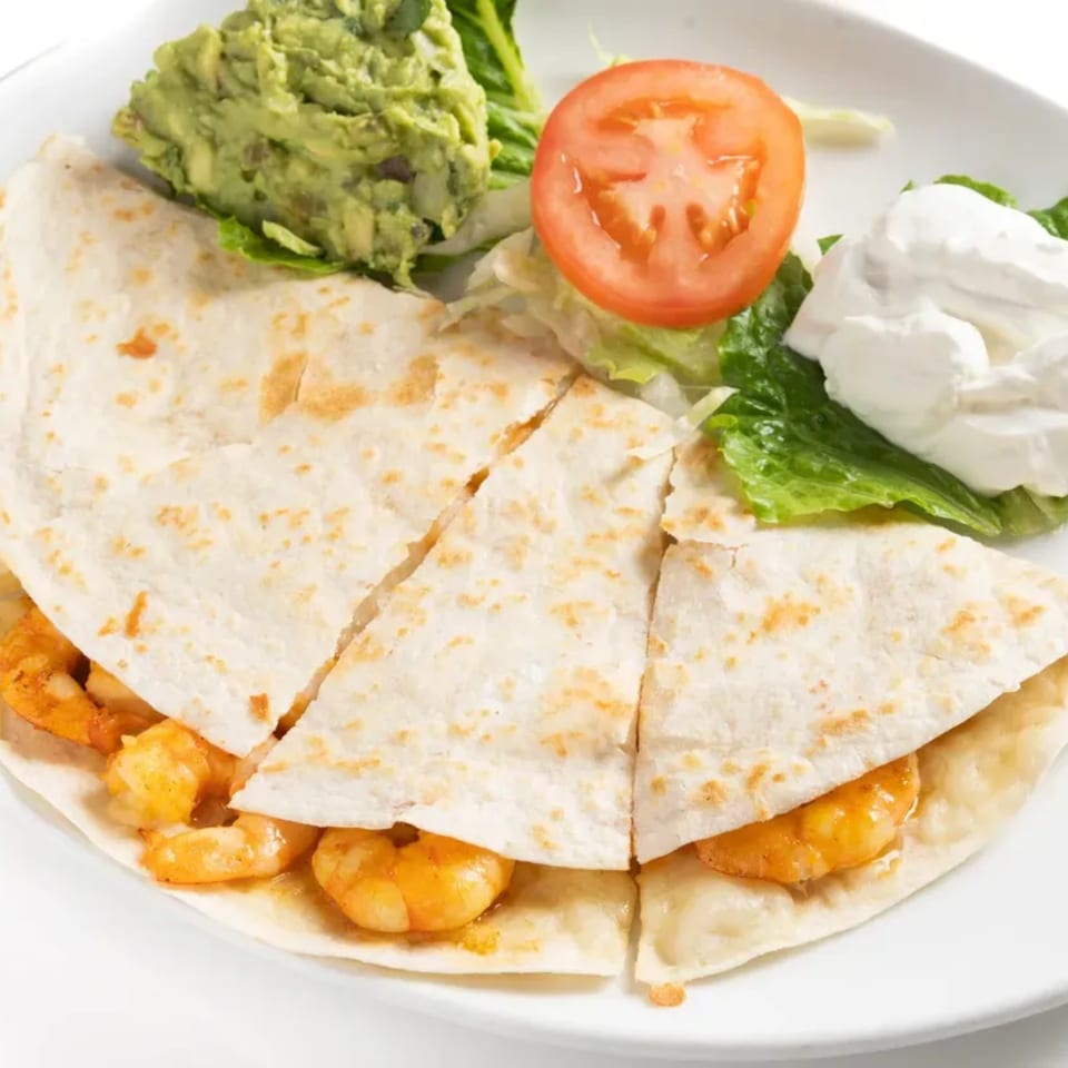 Shrimp quesadilla with guacamole, sour cream, lettuce, and a tomato slice on a white plate.